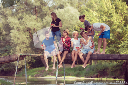 Image of friends enjoying watermelon while sitting on the wooden bridge