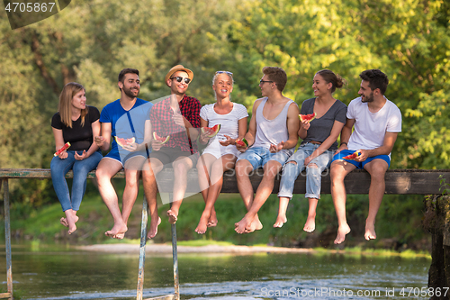 Image of friends enjoying watermelon while sitting on the wooden bridge