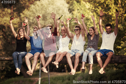 Image of friends enjoying watermelon while sitting on the wooden bridge