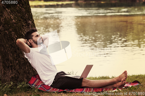 Image of man using a laptop computer on the bank of the river