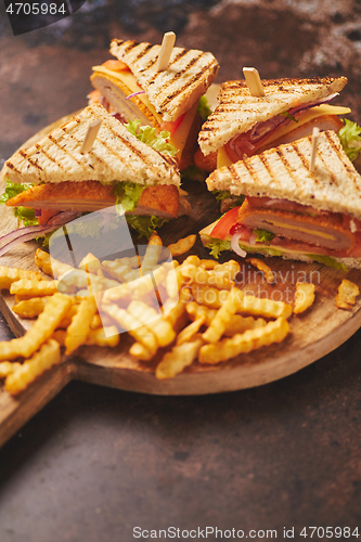 Image of Club sandwiches served on a wooden board. With hot French fries