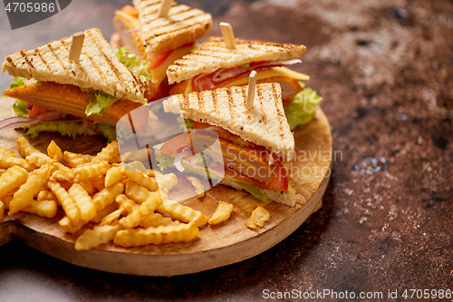 Image of Club sandwiches served on a wooden board. With hot French fries