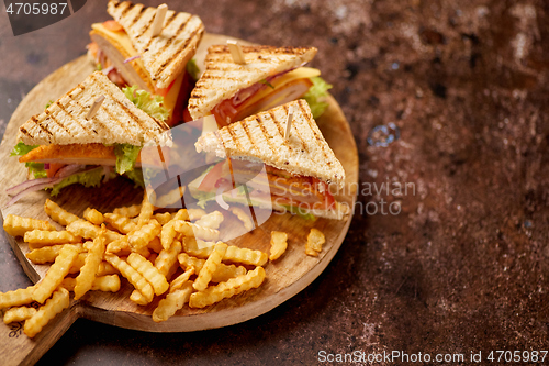 Image of Chicken and cheese club sandwiches served on a wooden board with french fries