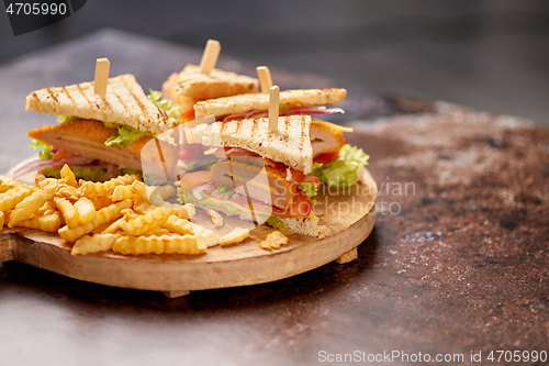 Image of Chicken and cheese club sandwiches served on a wooden board with french fries