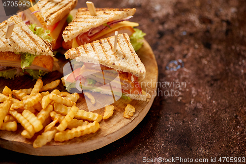 Image of Club sandwiches served on a wooden board. With hot French fries