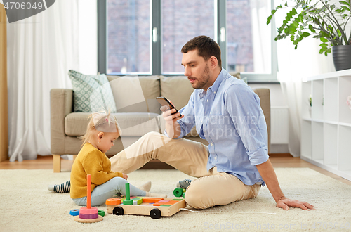 Image of father with smartphone and baby daughter at home