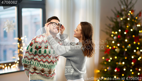 Image of happy couple in ugly sweaters at home on christmas