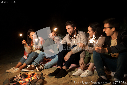 Image of happy friends with sparklers at camp fire at night