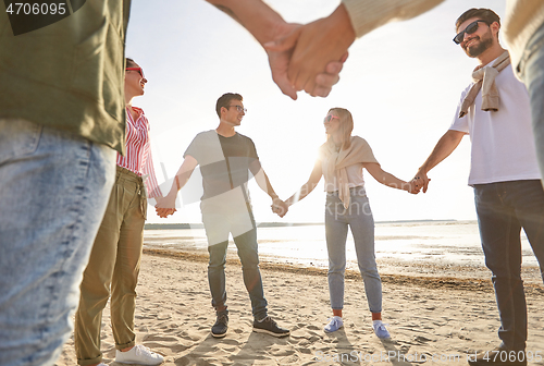 Image of happy friends holding hands on summer beach