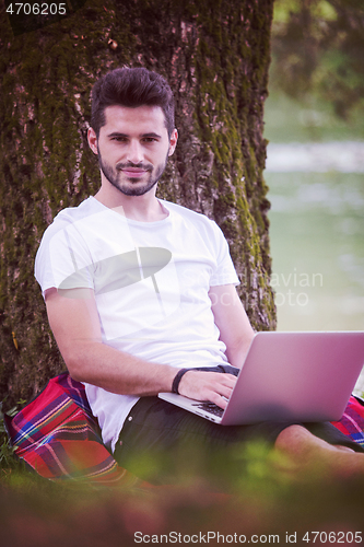 Image of man using a laptop computer on the bank of the river