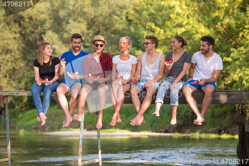 Image of friends enjoying watermelon while sitting on the wooden bridge