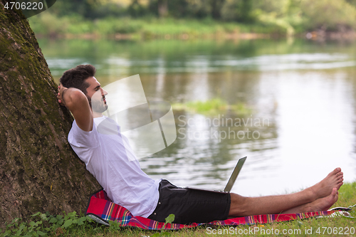 Image of man using a laptop computer on the bank of the river