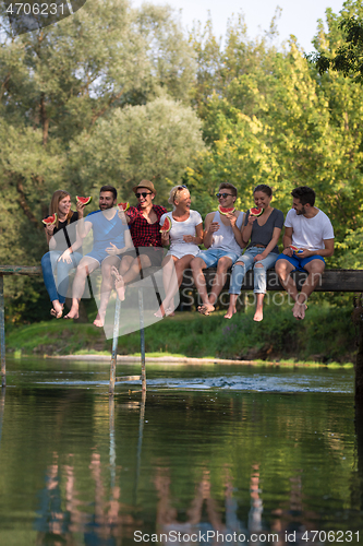 Image of friends enjoying watermelon while sitting on the wooden bridge