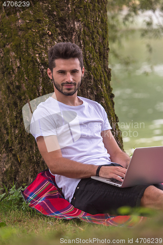 Image of man using a laptop computer on the bank of the river