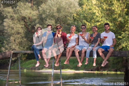 Image of friends enjoying watermelon while sitting on the wooden bridge