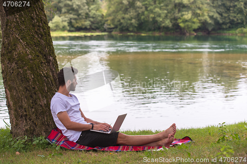 Image of man using a laptop computer on the bank of the river