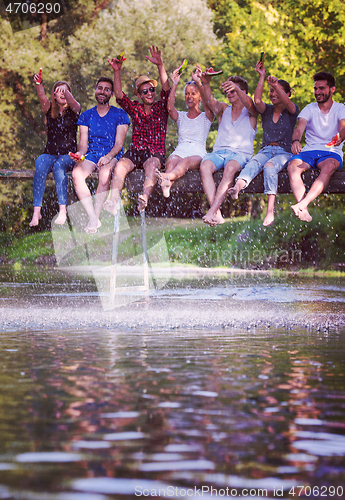 Image of friends enjoying watermelon while sitting on the wooden bridge