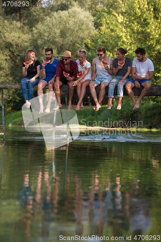 Image of friends enjoying watermelon while sitting on the wooden bridge