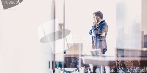 Image of Businessman talking on a mobile phone in corporate office while looking through window.