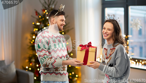 Image of happy couple in christmas sweaters with gift box