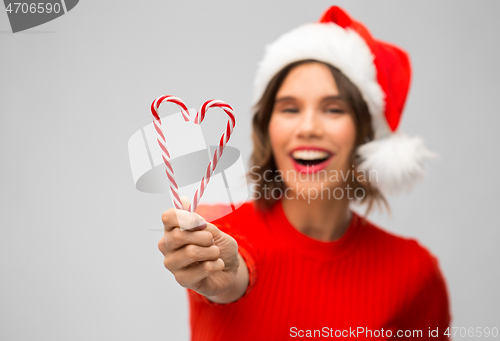 Image of happy woman in santa hat showing candy canes