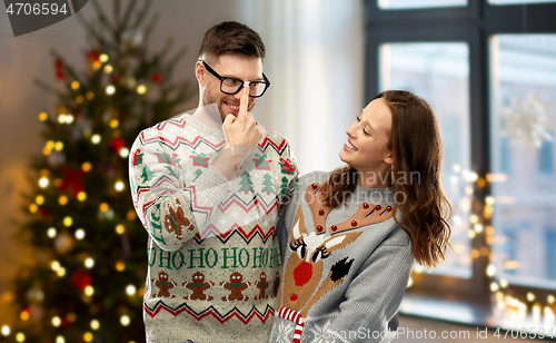 Image of happy couple in christmas ugly sweaters at home