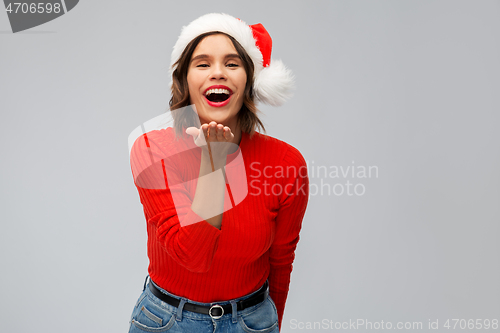 Image of happy young woman in santa hat sending air kiss