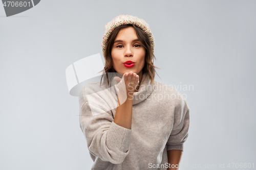 Image of young woman in knitted winter hat sending air kiss