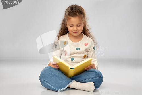 Image of beautiful smiling girl reading book on floor