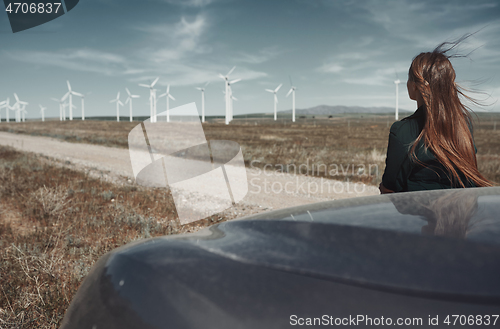 Image of Woman leaning to her car next to the wind turbines site