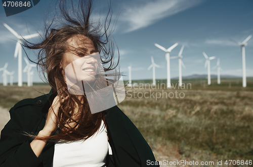 Image of Woman with long tousled hair next to the wind turbine with the w