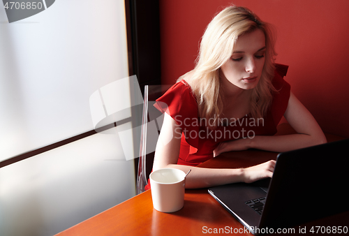 Image of Young adult woman wearing red jumpsuit and using laptop