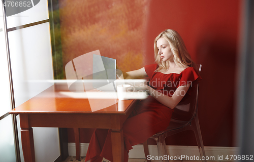 Image of Young adult woman sitting at the table and working on laptop