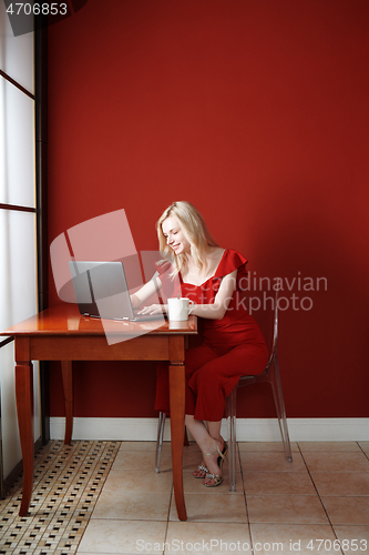 Image of Young adult woman sitting at the table and working on laptop