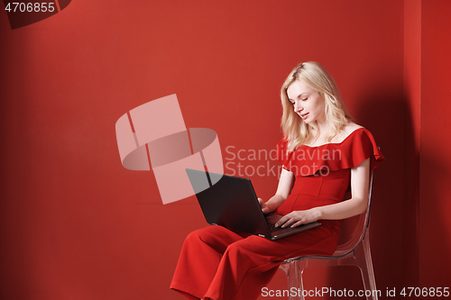 Image of Young adult woman sitting on a chair and working on laptop