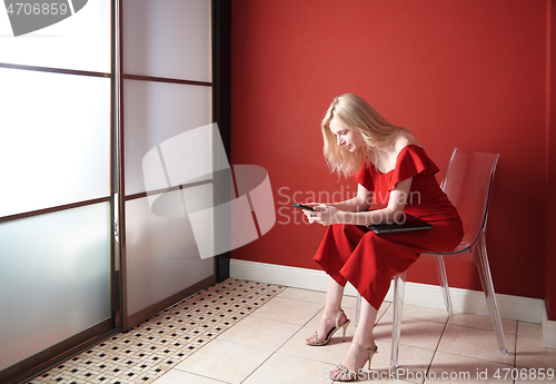 Image of Young adult woman using smartphone and holding laptop