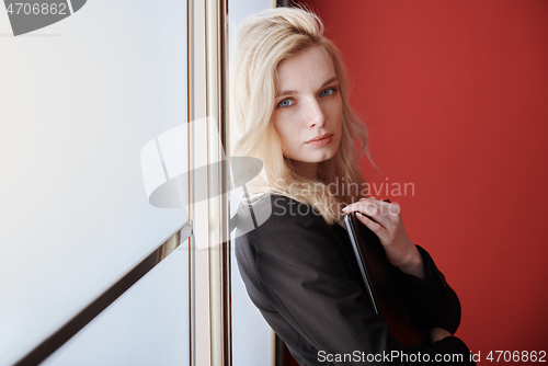 Image of Young adult business woman standing next to the window holding l