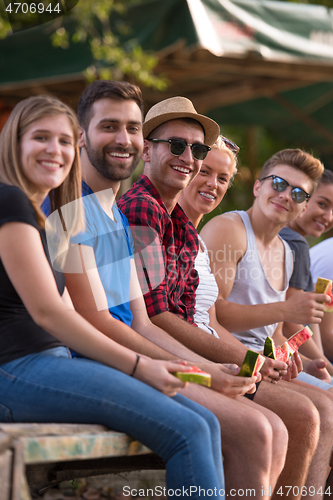 Image of friends enjoying watermelon while sitting on the wooden bridge