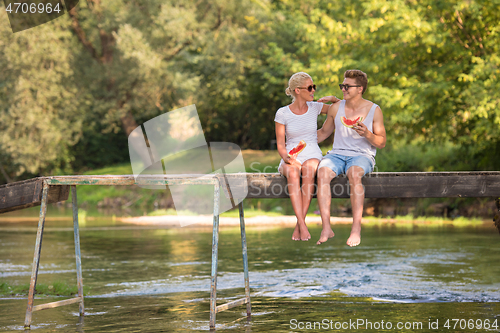 Image of couple enjoying watermelon while sitting on the wooden bridge