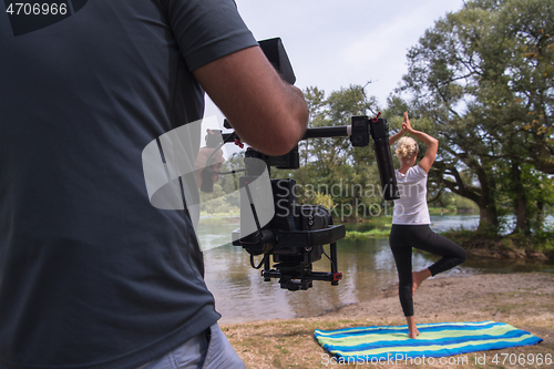 Image of young videographer recording while woman doing yoga exercise