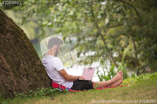 Image of man using a laptop computer on the bank of the river