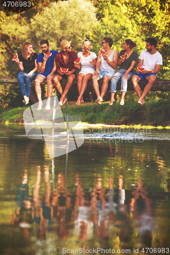 Image of friends enjoying watermelon while sitting on the wooden bridge