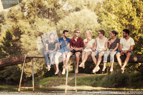 Image of friends enjoying watermelon while sitting on the wooden bridge