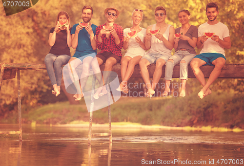 Image of friends enjoying watermelon while sitting on the wooden bridge