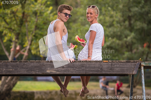 Image of couple enjoying watermelon while sitting on the wooden bridge