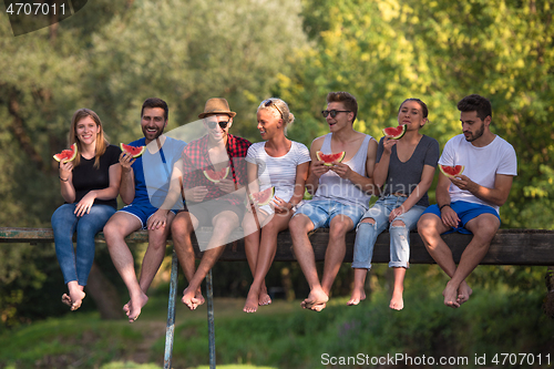 Image of friends enjoying watermelon while sitting on the wooden bridge