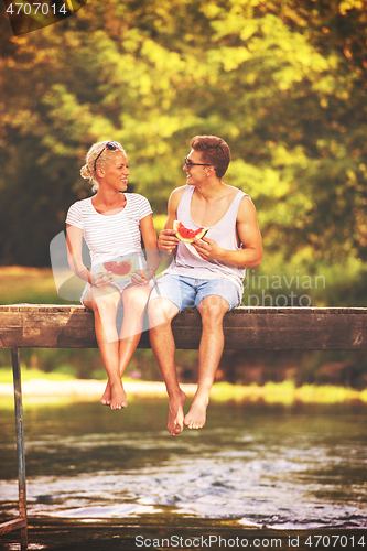 Image of couple enjoying watermelon while sitting on the wooden bridge