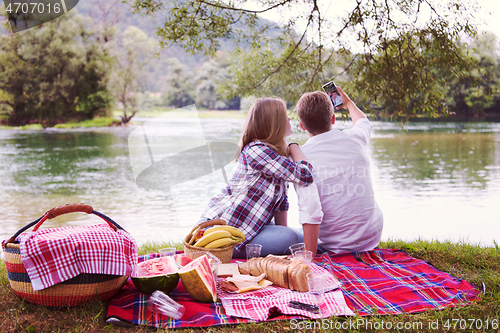 Image of Couple taking a selfie by mobile phone while enjoying picnic tim