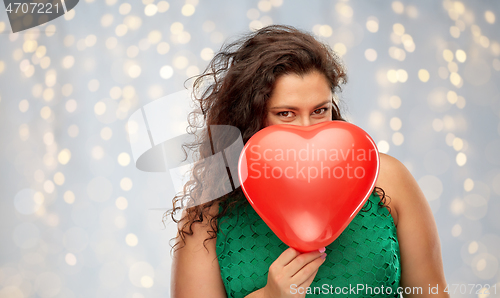 Image of playful woman holding red heart shaped balloon