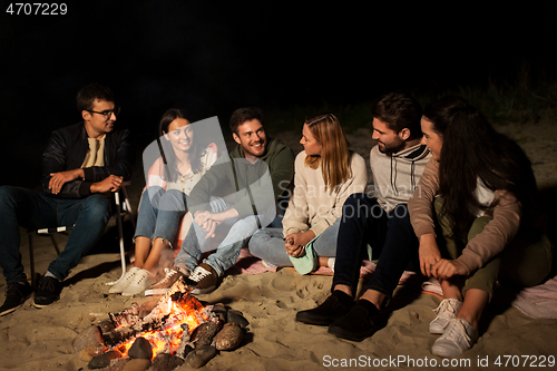 Image of group of friends sitting at camp fire on beach
